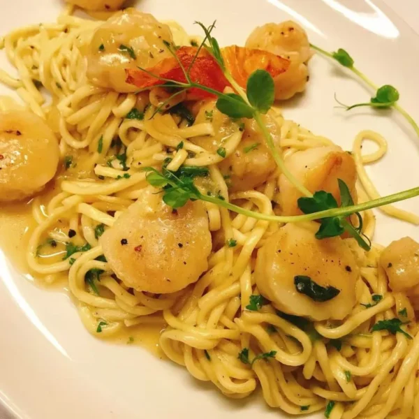 Pasta dish served on a white plate with herbs and vegetables