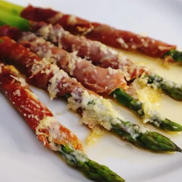 Asparagus wrapped in prosciutto with melted cheese served on a white plate.