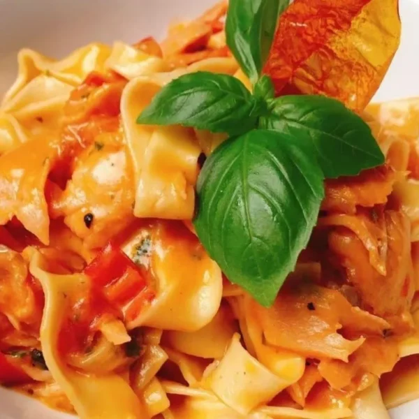 Handmade pasta with tomato sauce, vegetables and fresh basil served in a white bowl.