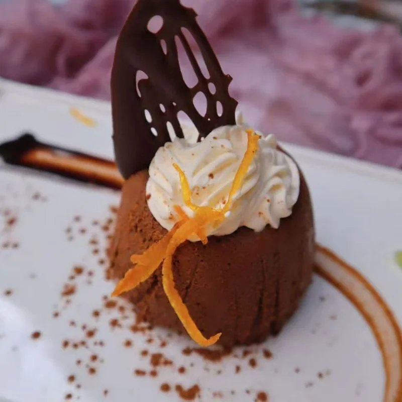 Chocolate dessert topped with whipped cream, chocolate decoration and orange zest on a white plate.