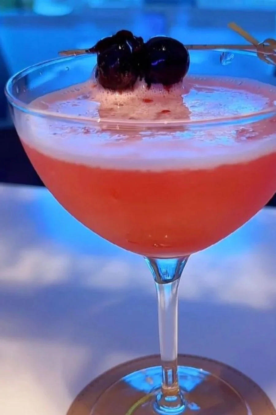 Pink cocktail served in a martini glass with cherry garnish